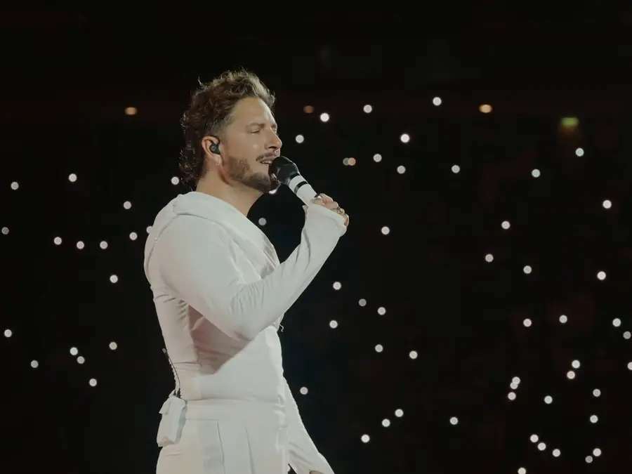 Manuel Carrasco, vestido de blanco, canta entre las luces de los móviles en La Cartuja, en 2026.