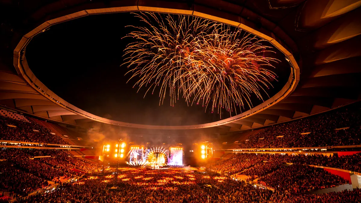 Fuegos artificiales sobre un estadio lleno, con el escenario encendido al fondo, en un concierto de Manuel Carrasco.
